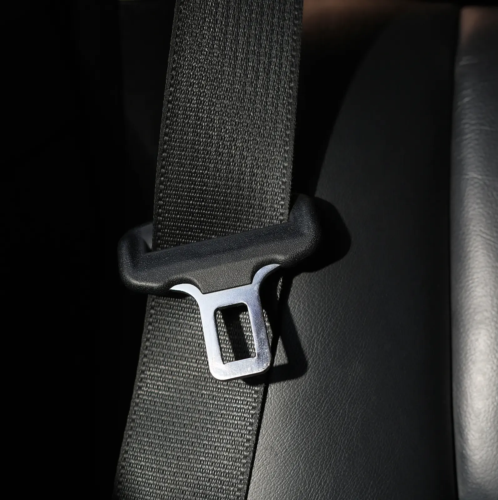 A seatbelt latch plate and webbing lit against a dark vehicle interior.