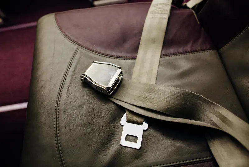 A two-point lap belt laid across a leather seat cushion, with its metal latch plate and buckle unfastened.