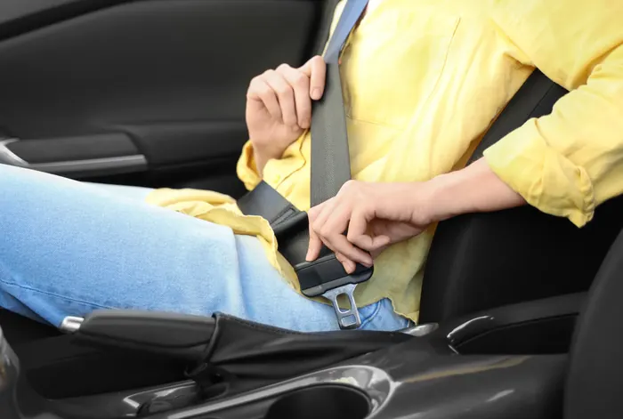 A person in a yellow shirt drawing a seatbelt across and guiding the latch plate towards the buckle inside a car.